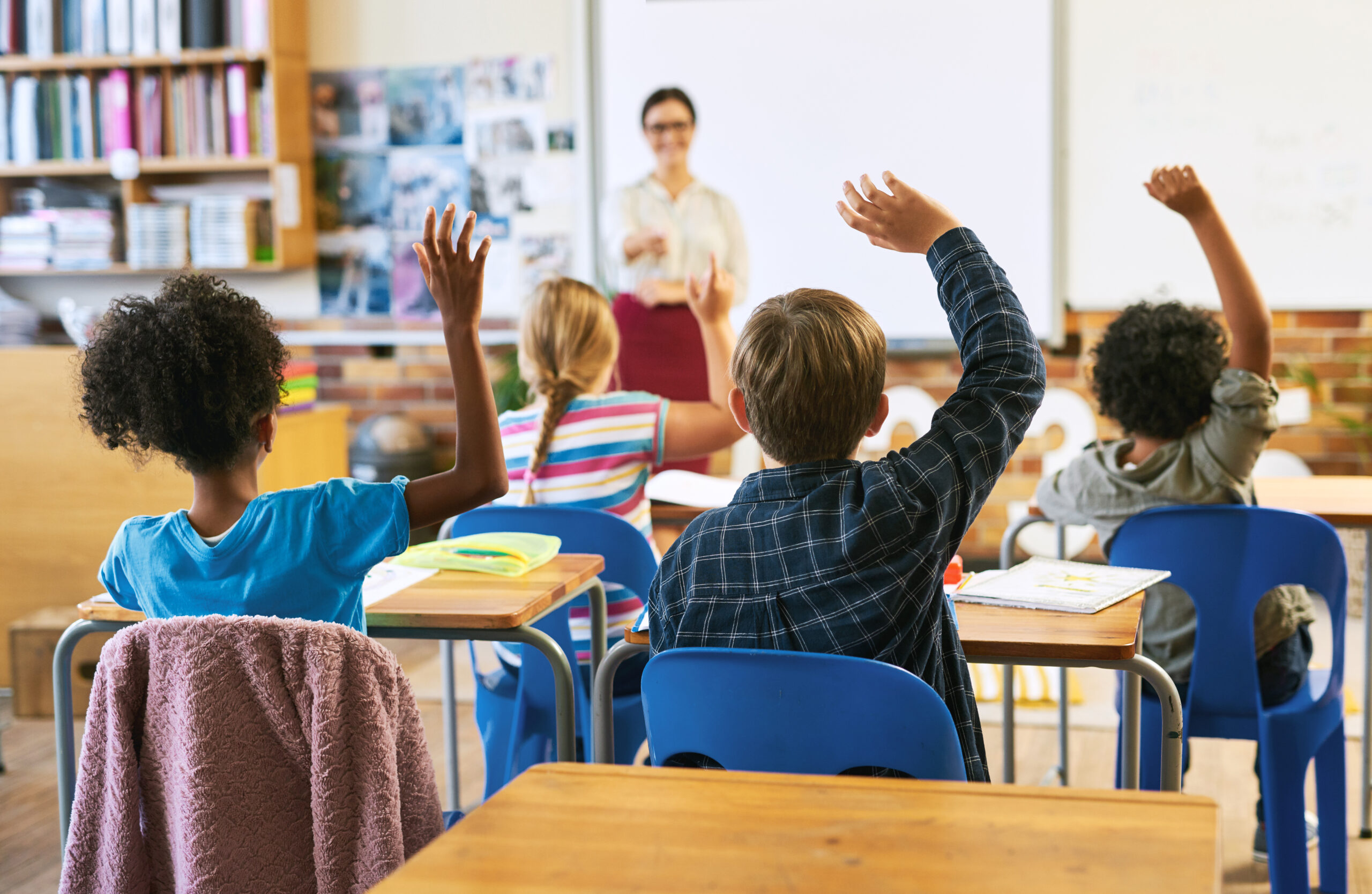 Group of children in classroom and raise their hands to answer